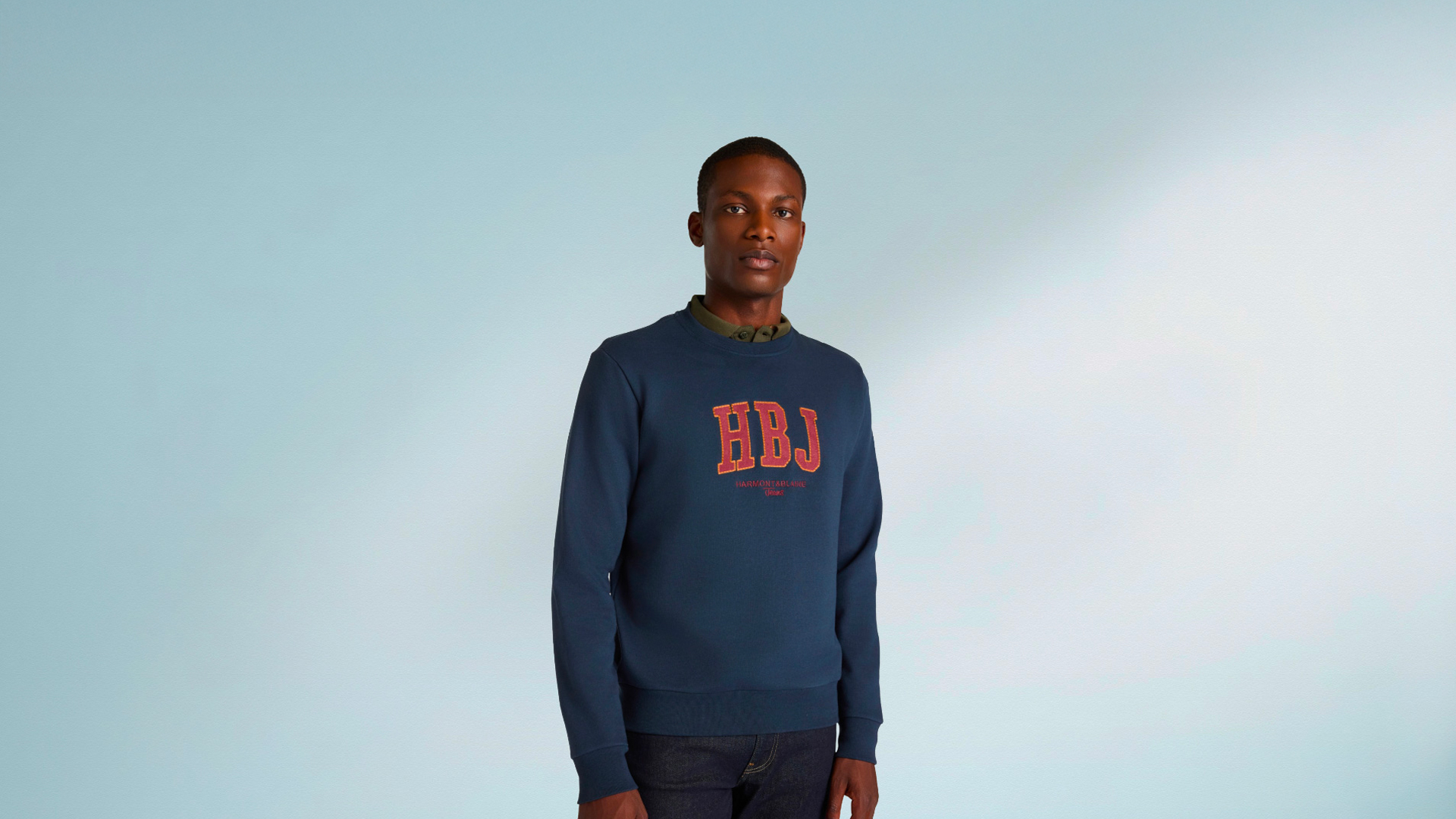 Felpa blu HBJ con logo ricamato e jeans scuri, immagine promozionale per i saldi HB Jeans.